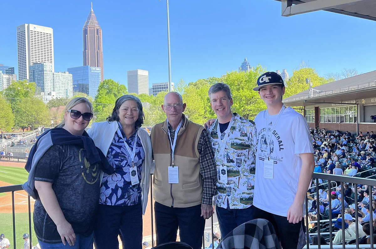 Five people posing together at a baseball game with a city skyline in the background.