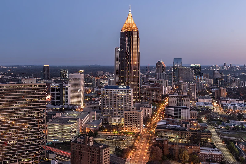 A city skyline at dusk features illuminated high-rise buildings with a prominent tower, and streets glowing with lights.