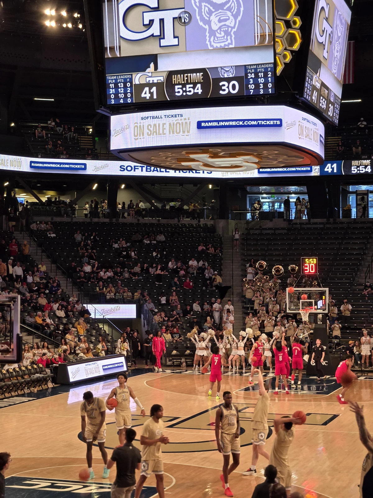 A college basketball game is taking place in a large indoor arena, with the scoreboard showing a halftime score of 41-30.